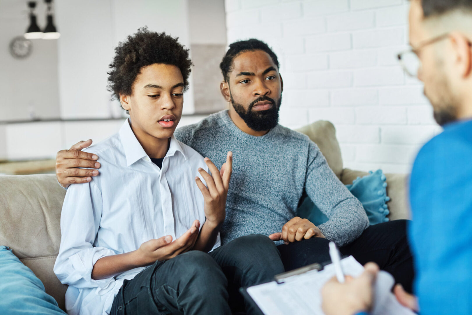 Father with his teenage son at meeting with social worker, psychologist discussing mental health family sitting on sofa in psychotherapist office